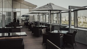 Un área de estar al aire libre con mobiliario de mimbre y sombrillas, con vistas a un paisaje urbano.