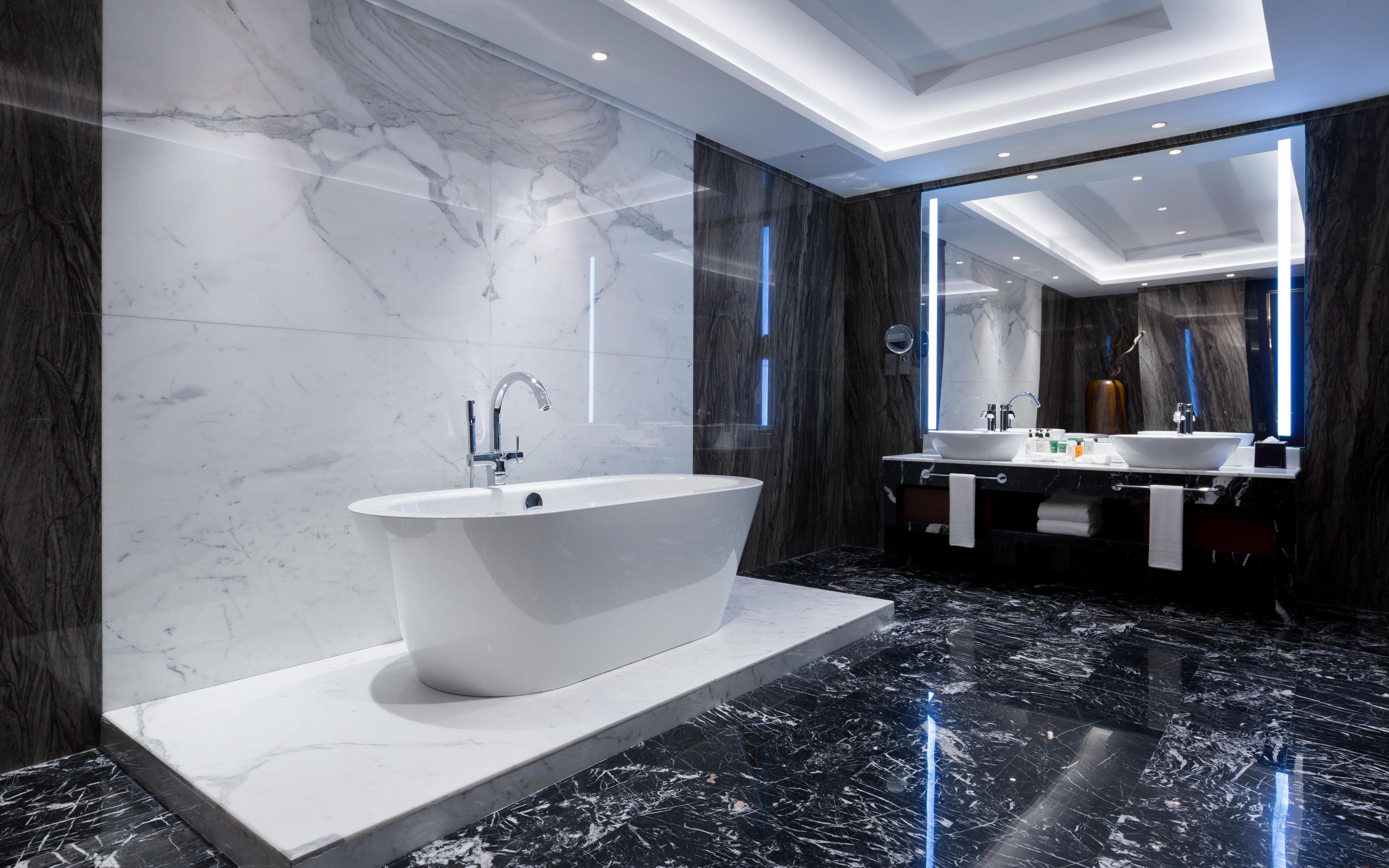 A modern bathroom with a freestanding bathtub, two sinks, and a large mirror.