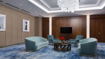 A modern room with a blue carpet, a chandelier, a flat-screen TV, and two sofas.