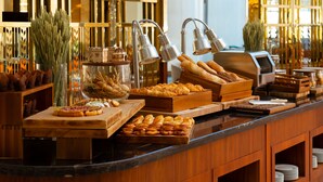 Un bufé con diversas opciones de panadería, incluyendo pasteles y pan, dispuestas en tablas y bandejas de madera.