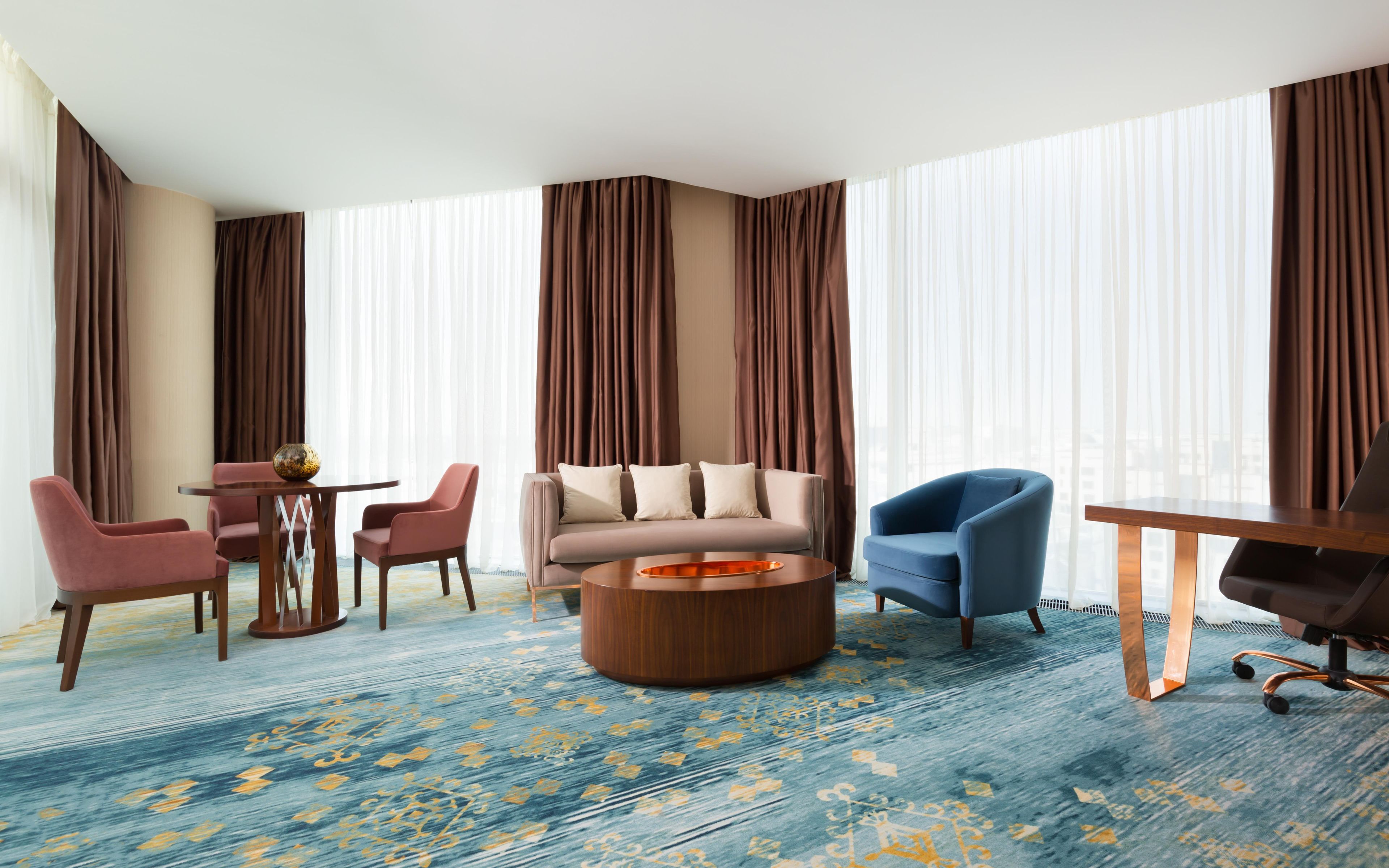A hotel room with a sofa, chairs, a coffee table, and a desk.