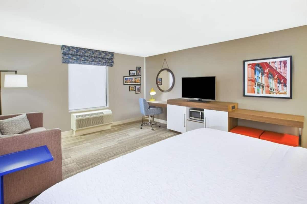 A hotel room with a bed, a desk, a chair, a television, and a window with blinds.