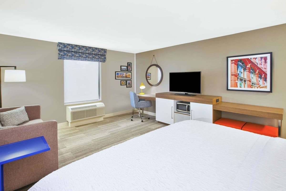 A hotel room with a bed, a desk, a chair, a TV, and a window.