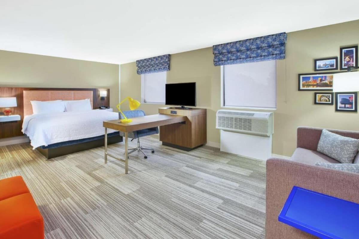 A hotel room with a bed, desk, chair, and a sofa.