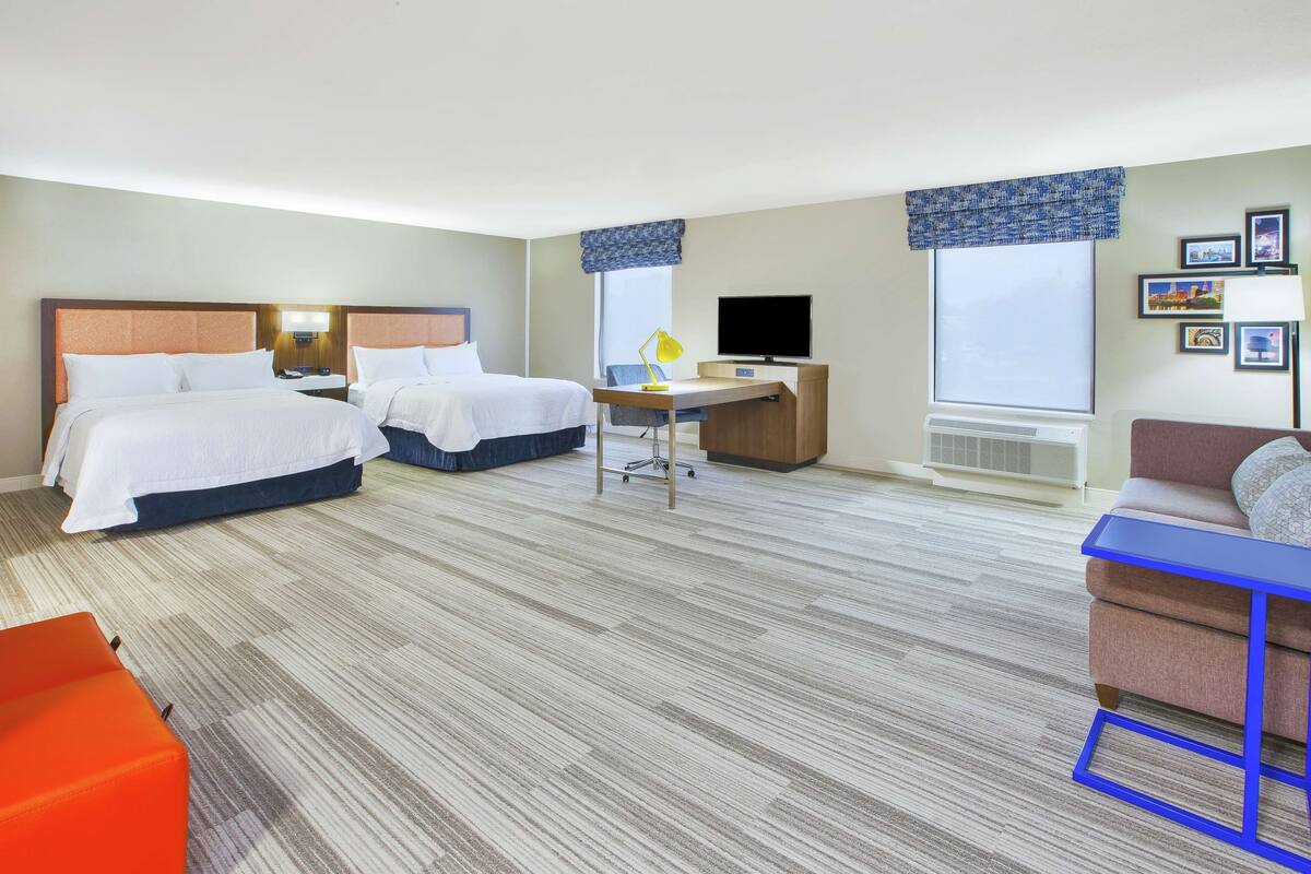 A hotel room with two beds, a desk, a TV, and a couch.