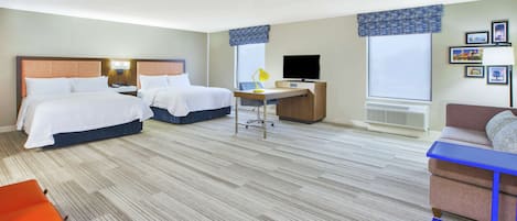 A hotel room with two beds, a desk, a TV, and a couch.