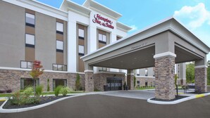Un hotel Hampton Inn & Suites con fachada moderna, entrada cubierta y área exterior ajardinada.