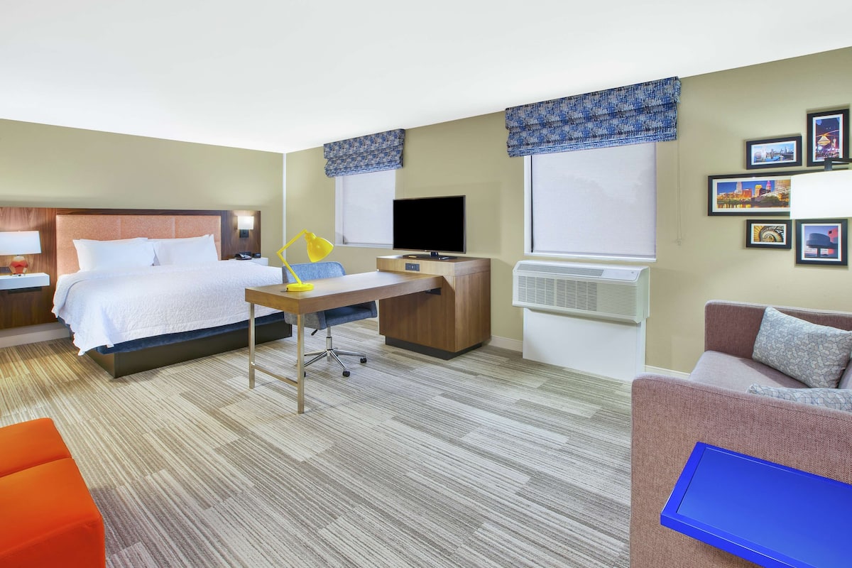 A hotel room with a bed, desk, chair, and a sofa.