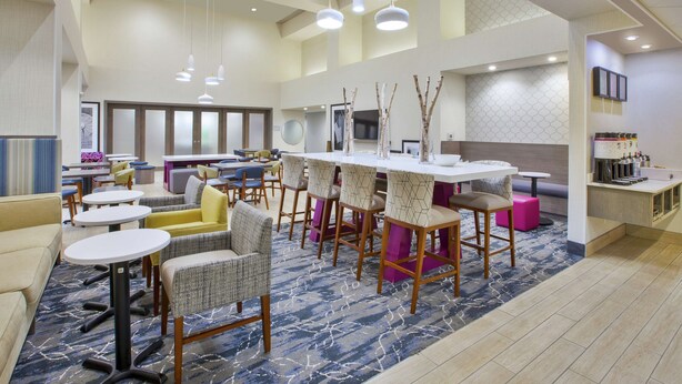 Un vestíbulo de hotel moderno con mesas redondas, taburetes de bar y una zona de estar.
