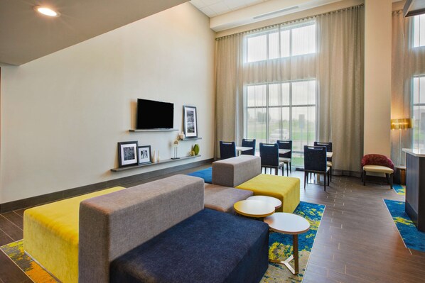 A modern hotel lobby with seating areas, a flat-screen TV, and large windows.