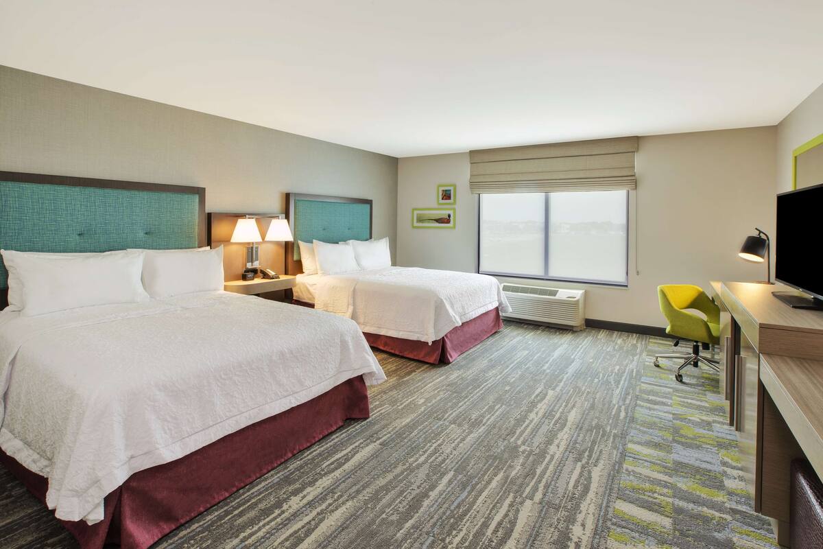 A hotel room with two beds, a desk, a chair, and a television.