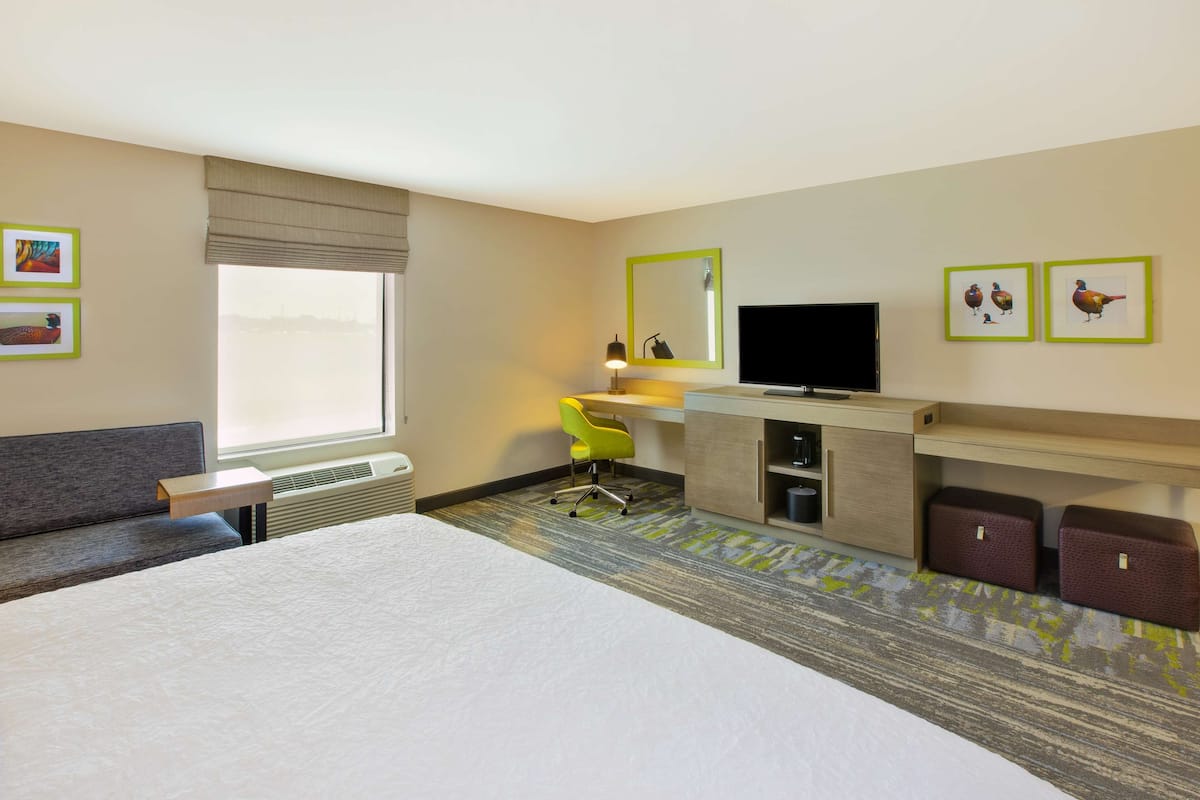 A hotel room with a large bed, a desk with a chair, a television, and artwork on the walls.