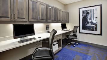 A conference room with a long table, two chairs, a desk with a computer, and a bookshelf.