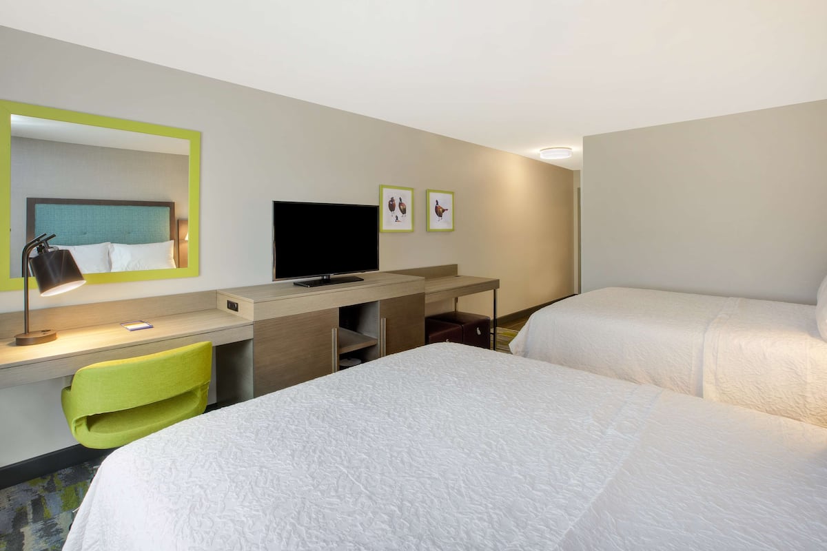 A hotel room with two beds, a desk with a chair, a television, and a mirror.