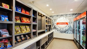 Uma área de exposição de lanches com diversos salgadinhos e bebidas, incluindo um refrigerador e uma placa com a inscrição 'Treats'.