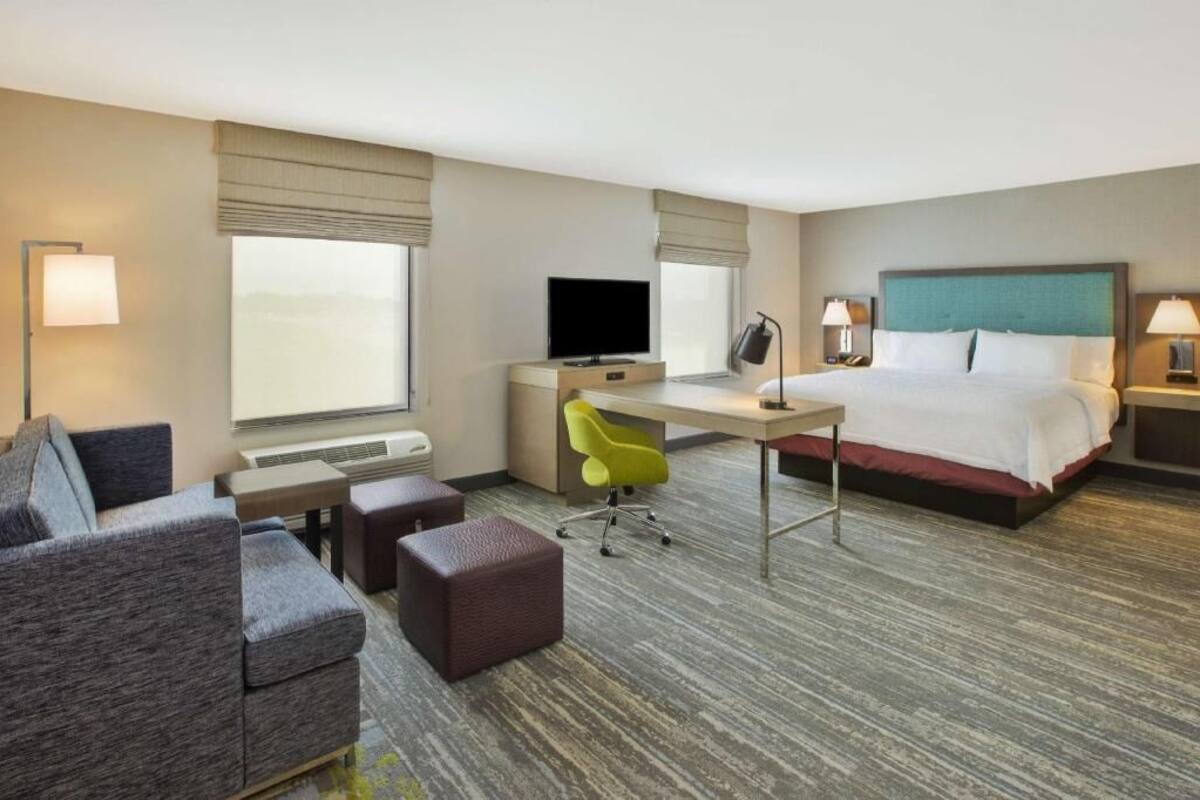 A hotel room with a bed, a desk with a chair, a television, and a sofa.