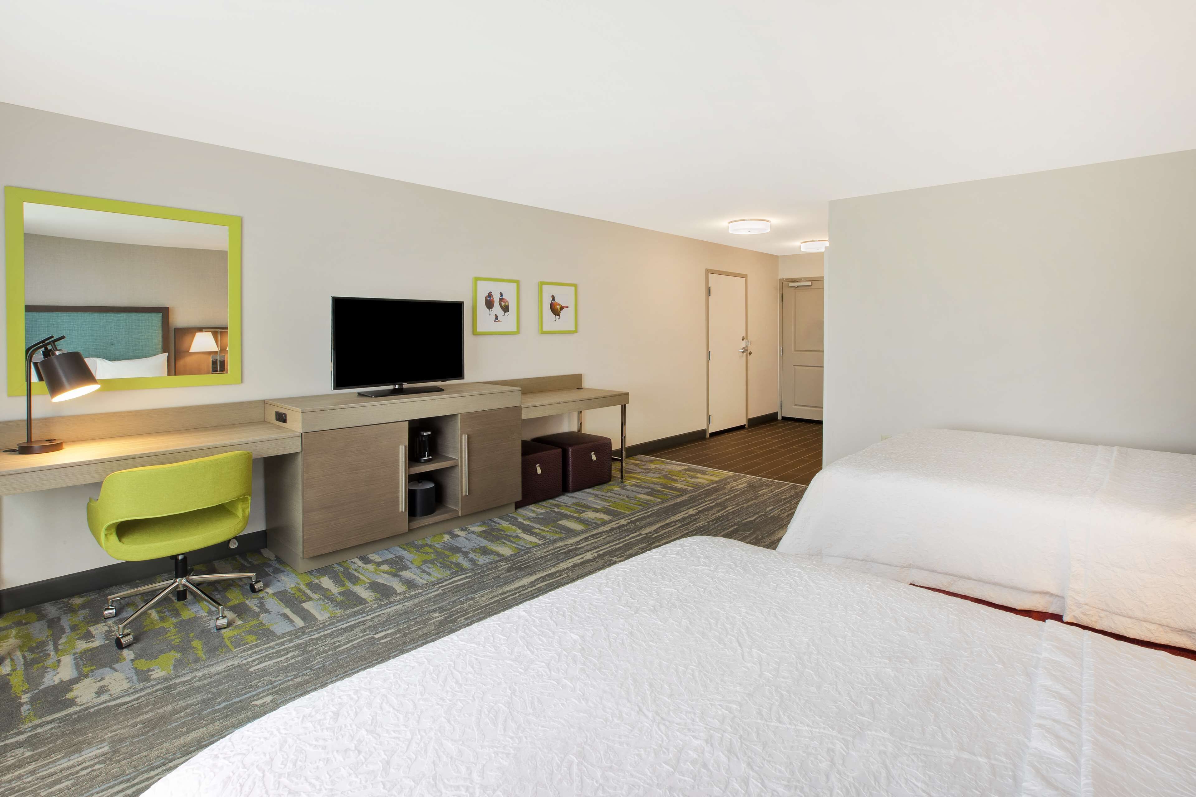 A hotel room with a bed, a desk with a chair, a television, and a door.