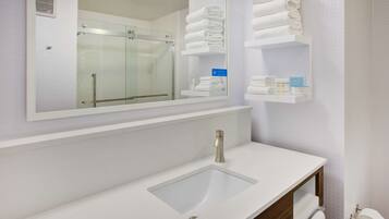 A modern bathroom with a glass shower, white sink, and towel storage.