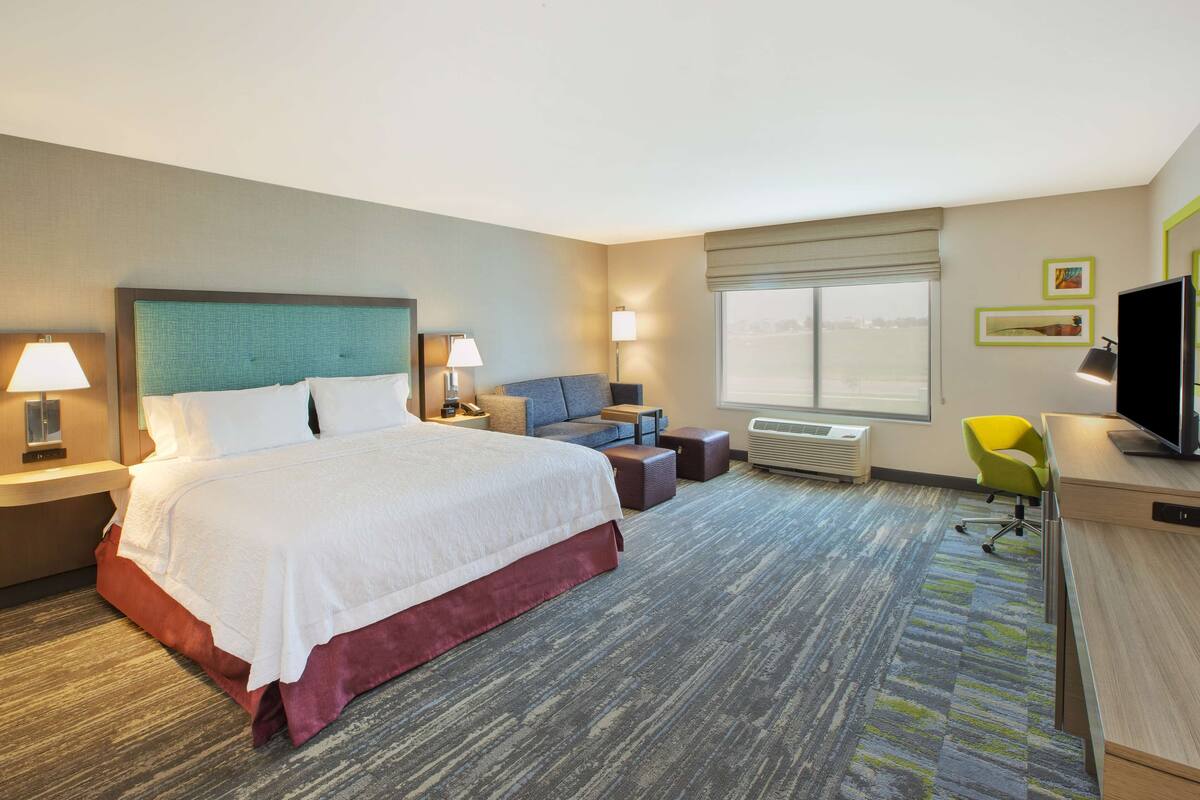 A hotel room with a large bed, a desk, a chair, a sofa, and a television.