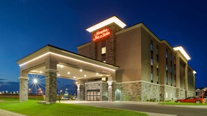 Um hotel Hampton Inn & Suites com uma entrada bem iluminada, uma área externa coberta e um céu noturno claro.