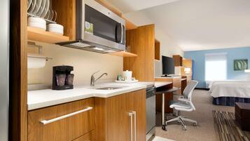 Habitación de hotel compacta con kitchenette, una cama, un escritorio y una silla.