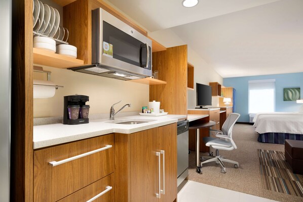 Habitación de hotel compacta con kitchenette, una cama, un escritorio y una silla.