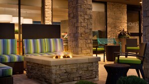 Un área de estar al aire libre con una chimenea de piedra, muebles de mimbre y vista al interior del hotel.