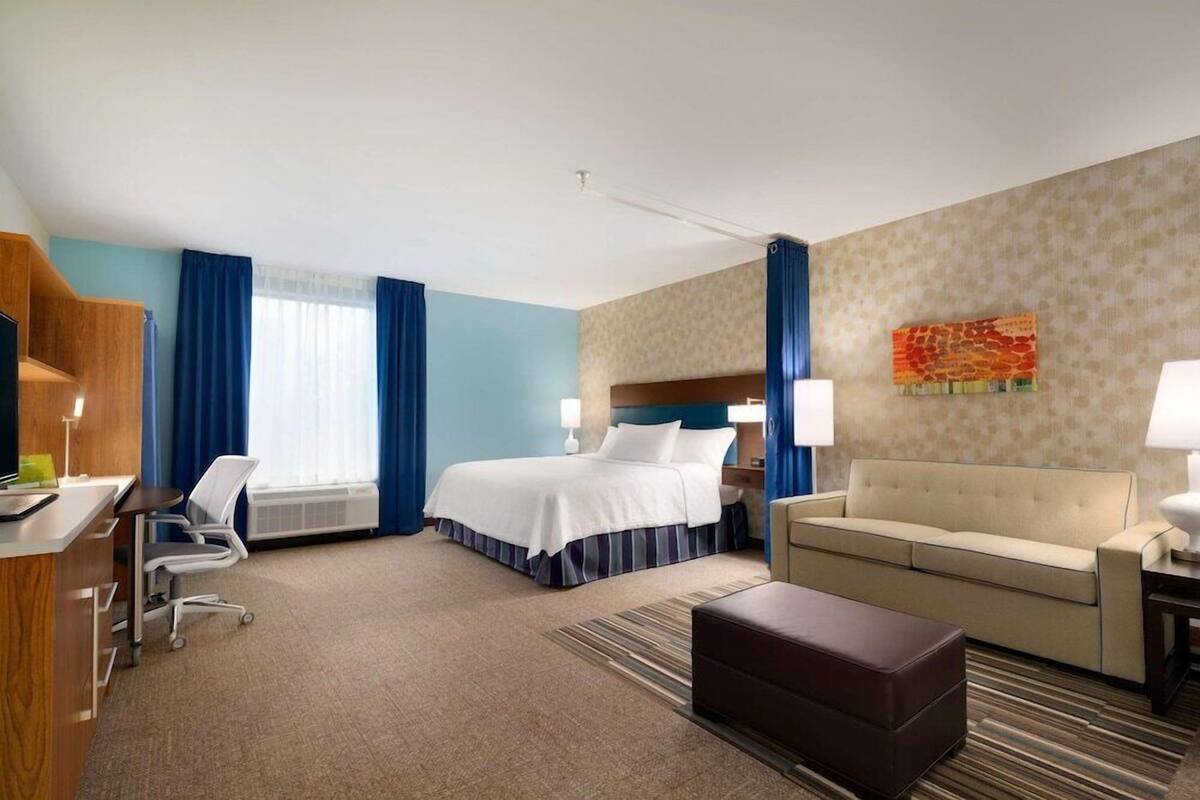 Une chambre d’hôtel comprenant un lit, un canapé, un bureau avec une chaise et une fenêtre avec des rideaux.