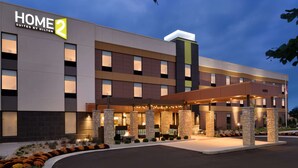 A modern hotel with a "HOME 2 Suites by Hilton" sign, outdoor seating area, and a well-lit entrance.