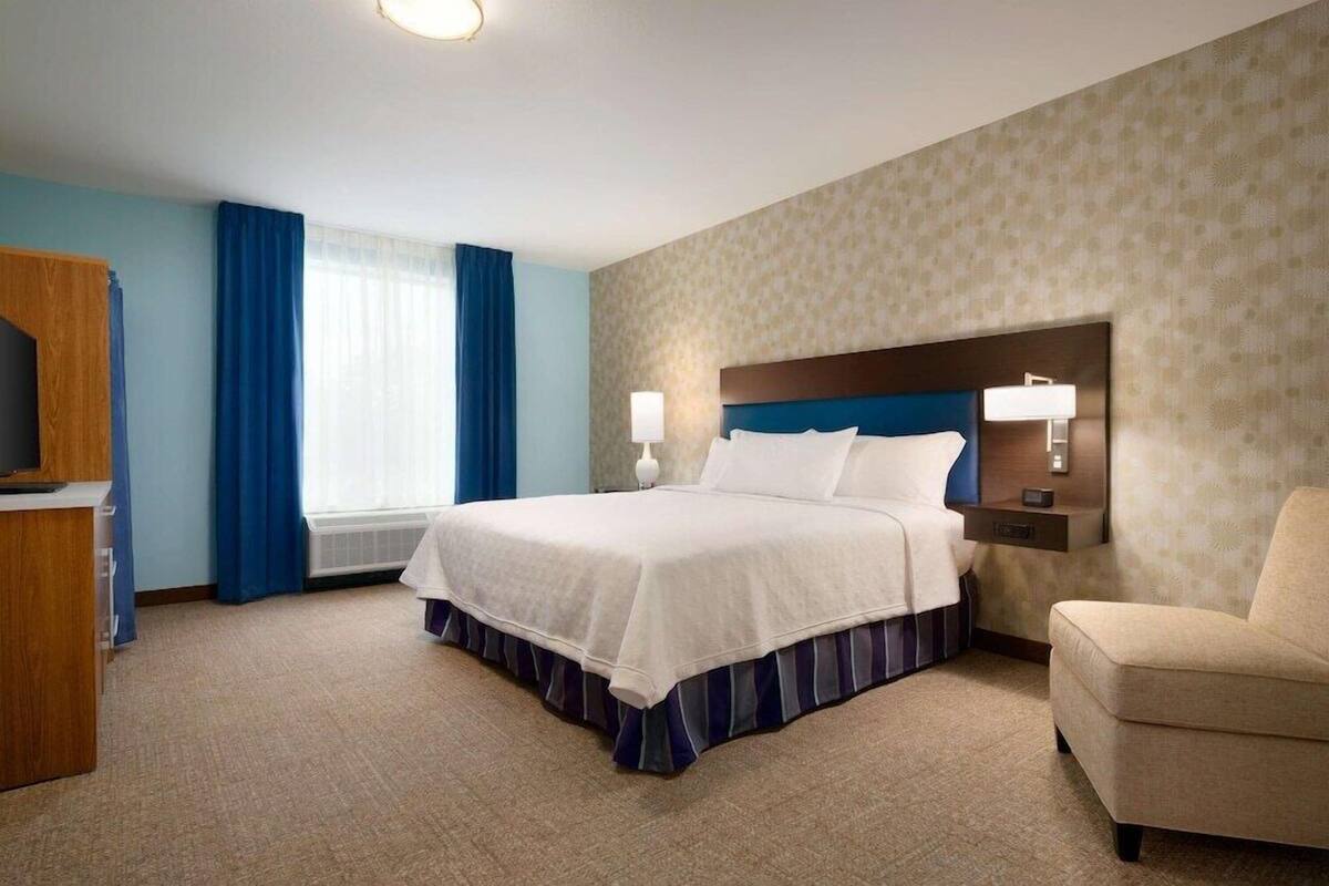 Une chambre d’hôtel avec un grand lit, un bureau, une chaise et une fenêtre avec des rideaux.