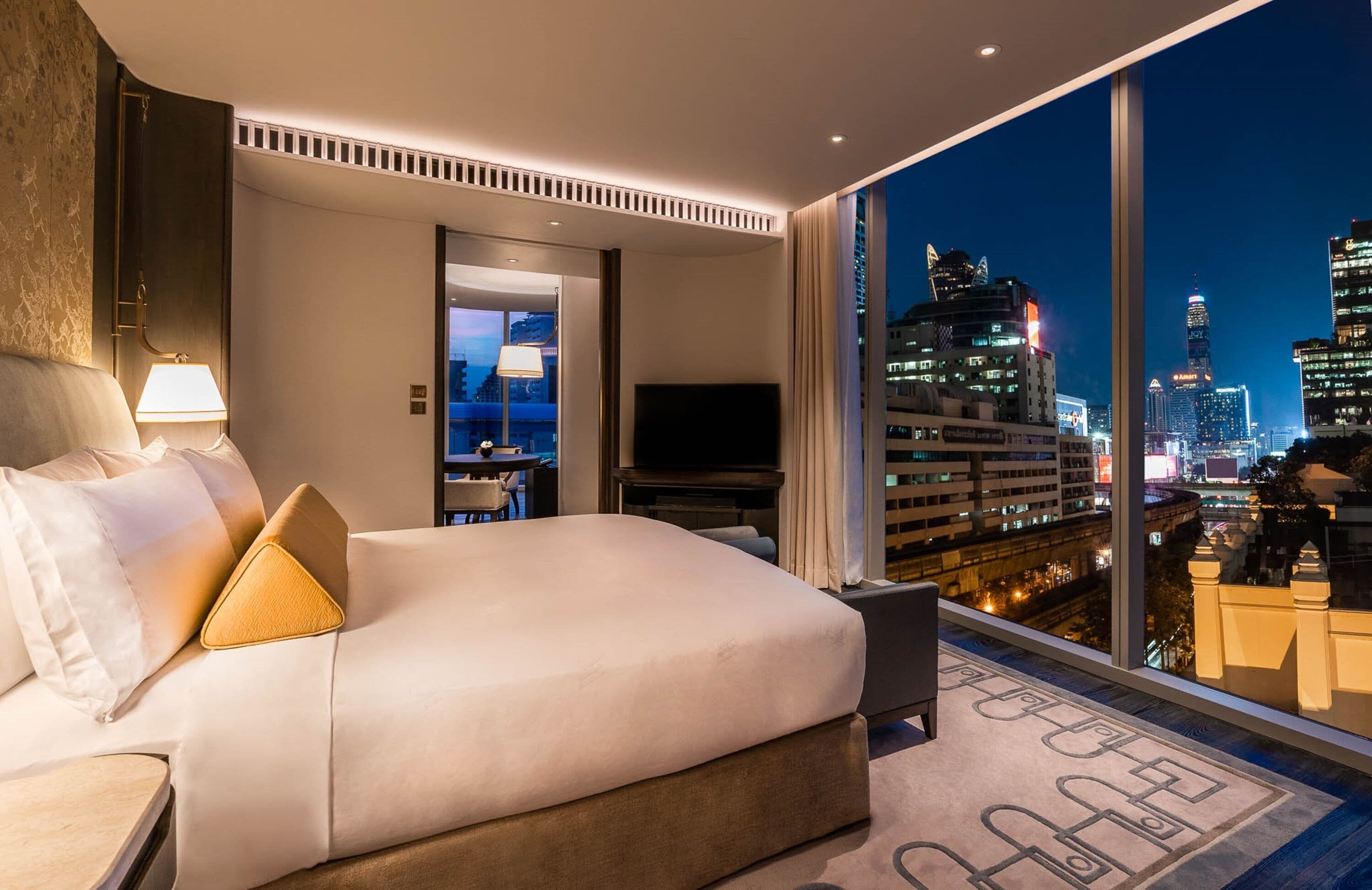 A modern hotel room with a large bed, a flat-screen TV, and a city view.