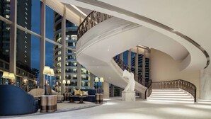 Een moderne lobby met een gebogen trap, een zithoek en grote ramen met uitzicht op een stadsbeeld.