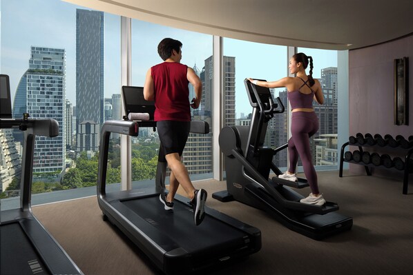 Dos personas ejercitándose en cintas de correr en una sala con ventanas amplias que dan a un paisaje urbano.