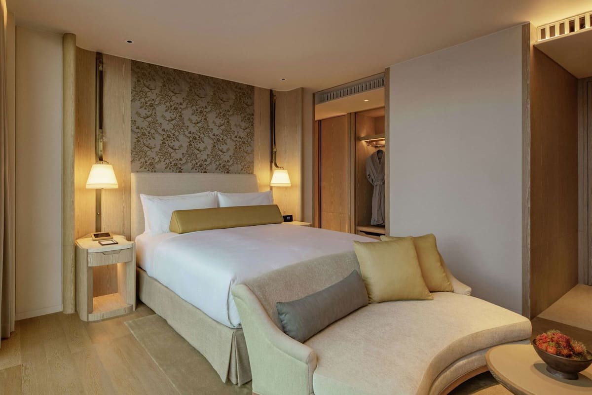 Een hotelkamer met een bed, nachtkastjes, een stoel, een badjas en een tafeltje met een fruitschaal.