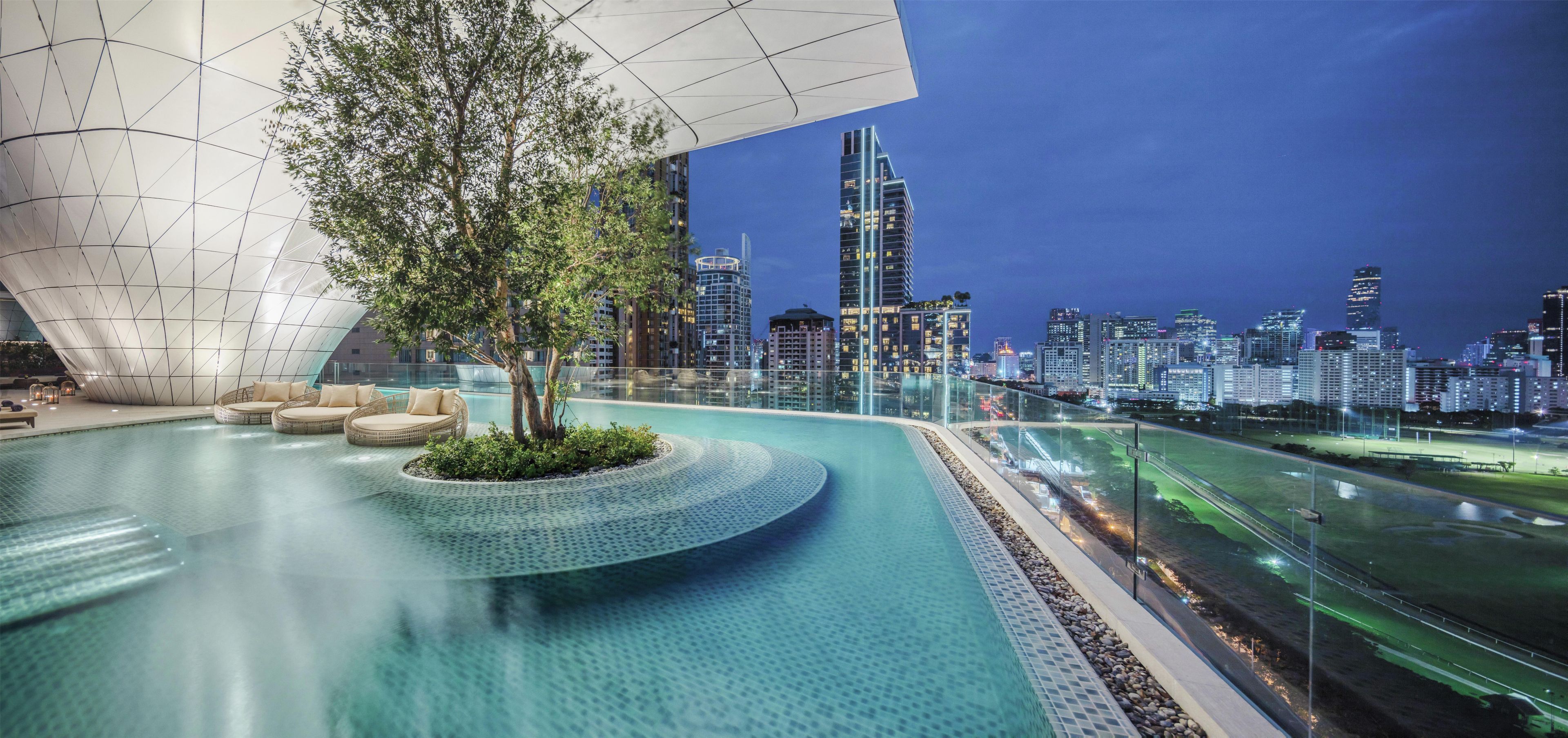 A modern pool area with a unique architectural design, surrounded by a city skyline at dusk.