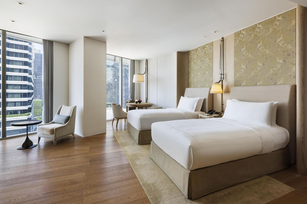 Een hotelkamer met twee bedden, een bureau, een stoel en grote ramen.
