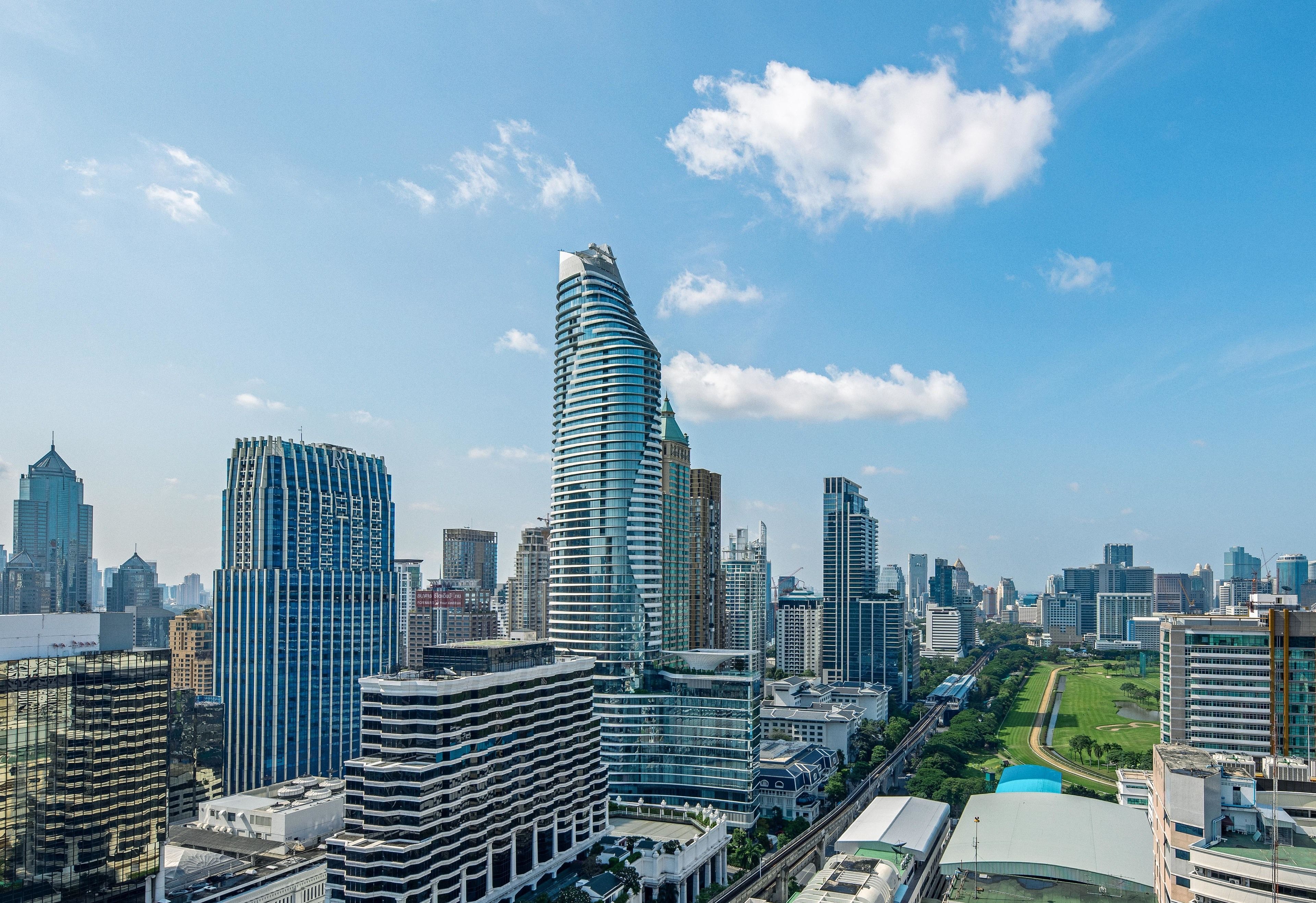 A cityscape with modern high-rise buildings, a prominent curved skyscraper, and a well-maintained park area.