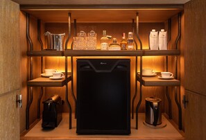 Una kitchenette compacta con refrigerador, cafetera y hervidor de agua.