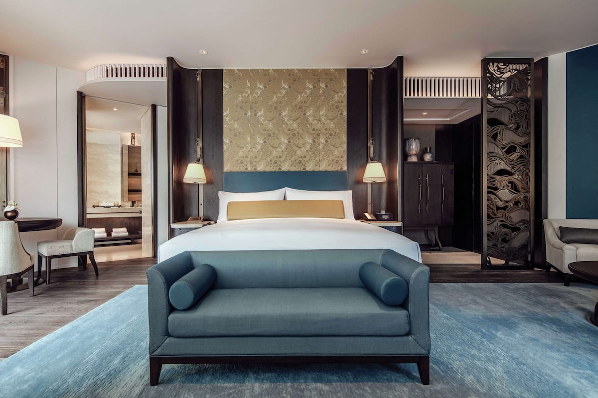 Een moderne hotelkamer met een groot bed, een bank, een bureau en een badkamer die door een open deur zichtbaar is.