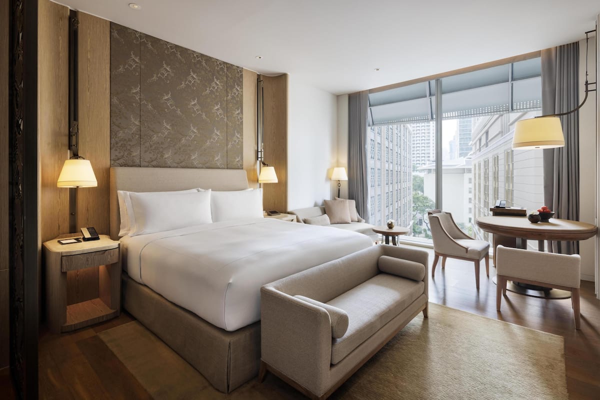 Een hotelkamer met een groot bed, nachtkastjes, een bank, een eettafel en uitzicht op de stad.