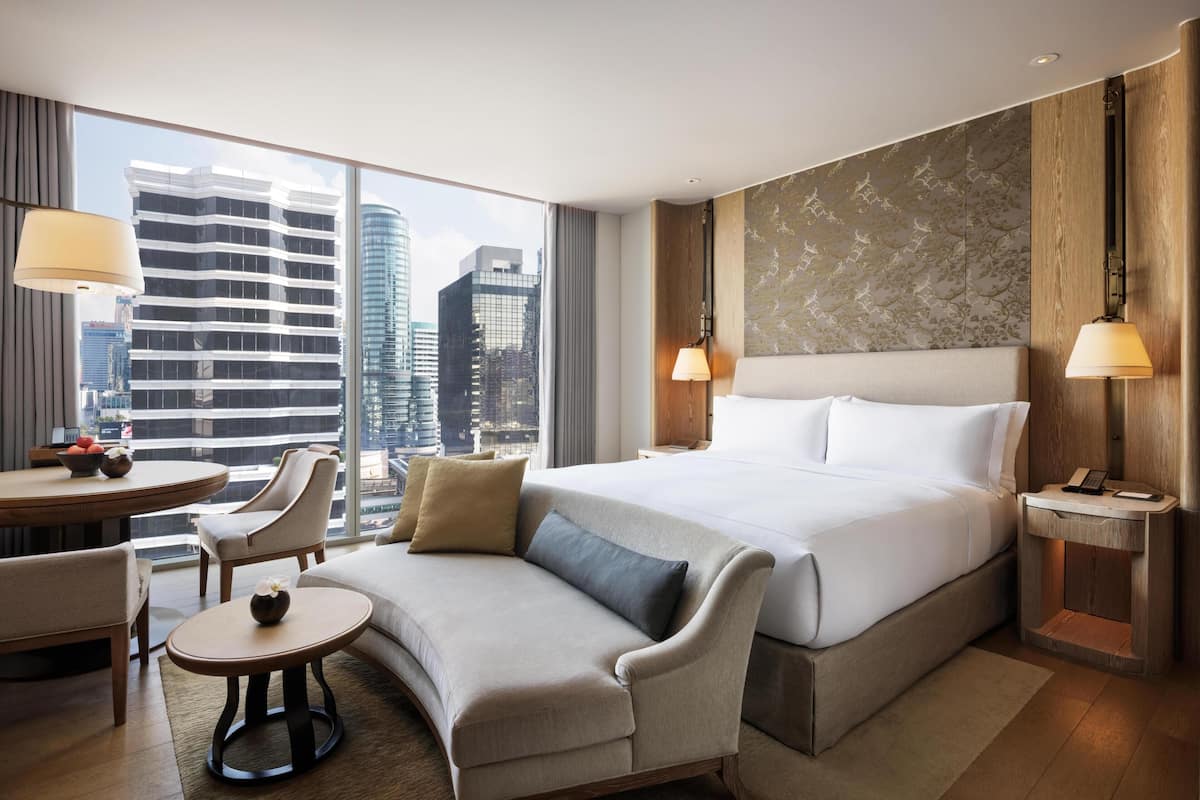 Een hotelkamer met een groot bed, een bank, een klein tafeltje en uitzicht op de stad.