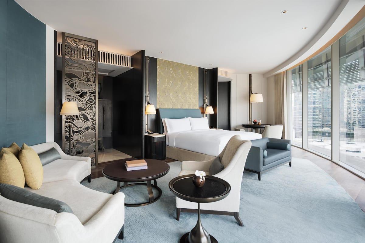 Een moderne hotelkamer met een groot bed, twee fauteuils, een tafeltje en uitzicht op de stad.