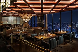 A high-rise restaurant with a city view, featuring leather seating, a chandelier, and a modern ceiling design. - Waldorf Astoria Bangkok (Bangkok)