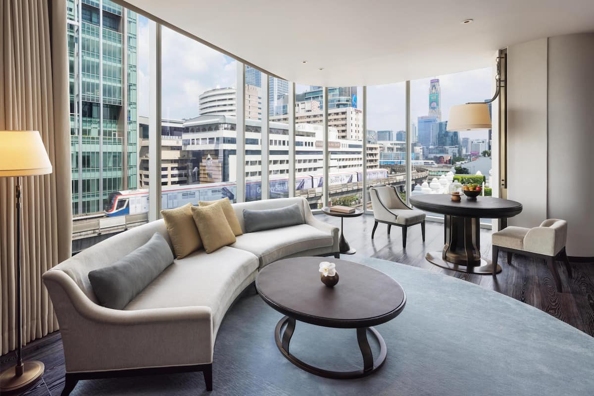 Een moderne hotelkamer met een gebogen bank, een ronde salontafel en uitzicht op de skyline door grote ramen.