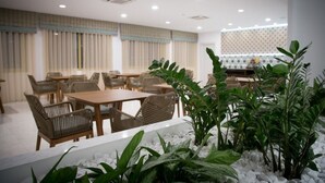 A dining area with tables and chairs, a plant in the foreground, and a patterned wall in the background. - Zephyros Hotel (Kalymnos)
