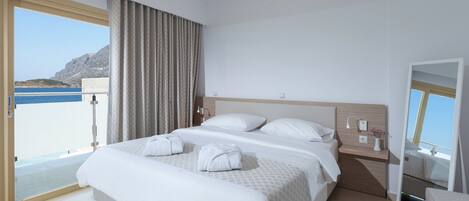 A hotel room with a large bed, a bedside table with a lamp, a mirror, and a view of the sea.