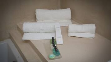 A bathroom with a bathtub, two white towels, a bottle of shampoo, and a box of toiletries.