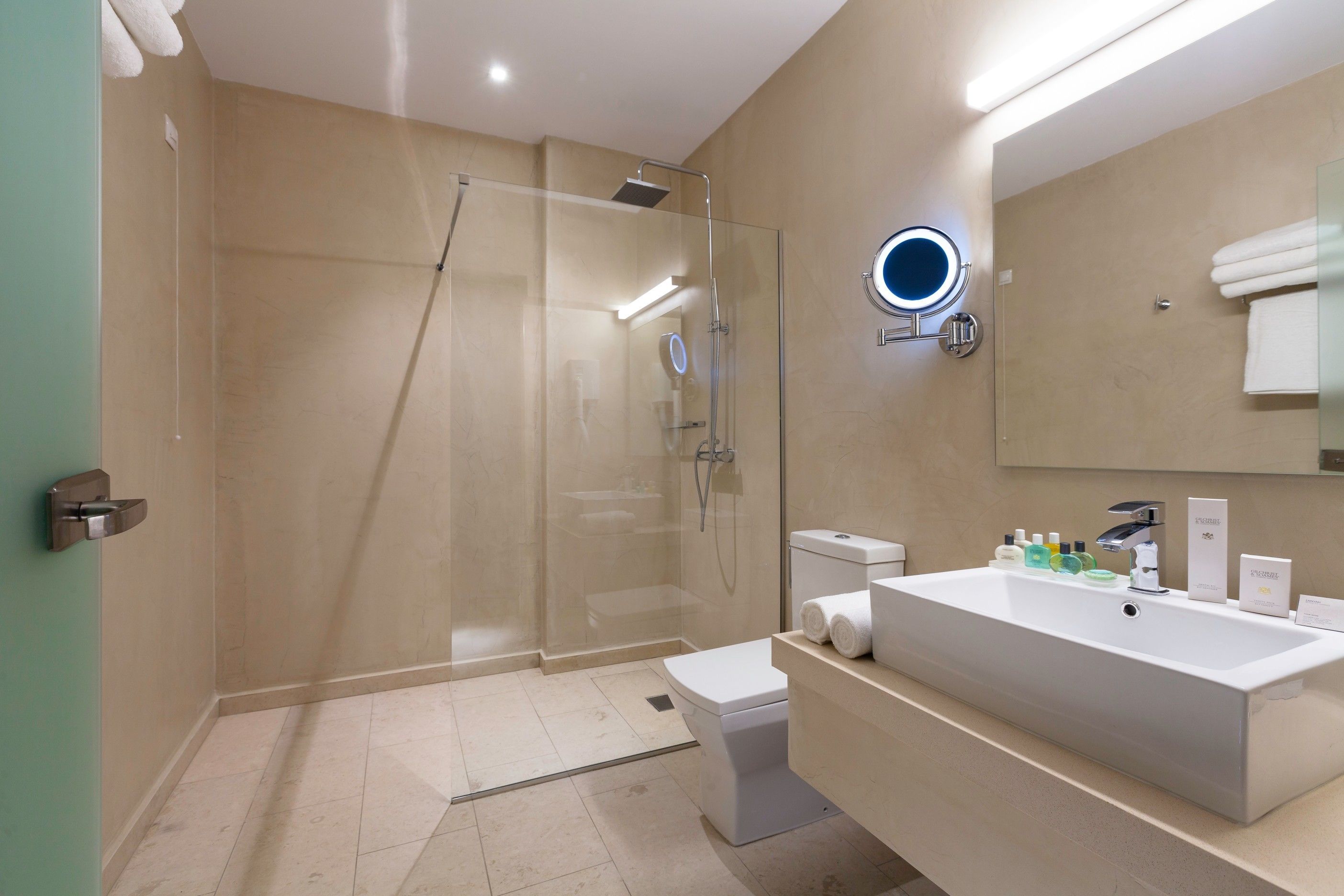 A modern bathroom with a glass-enclosed shower, a large sink, and a mirror with a built-in light.
