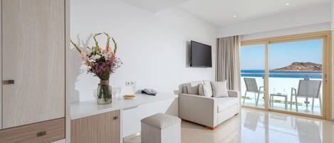 A modern living room with a sofa, a TV, and a view of the sea.