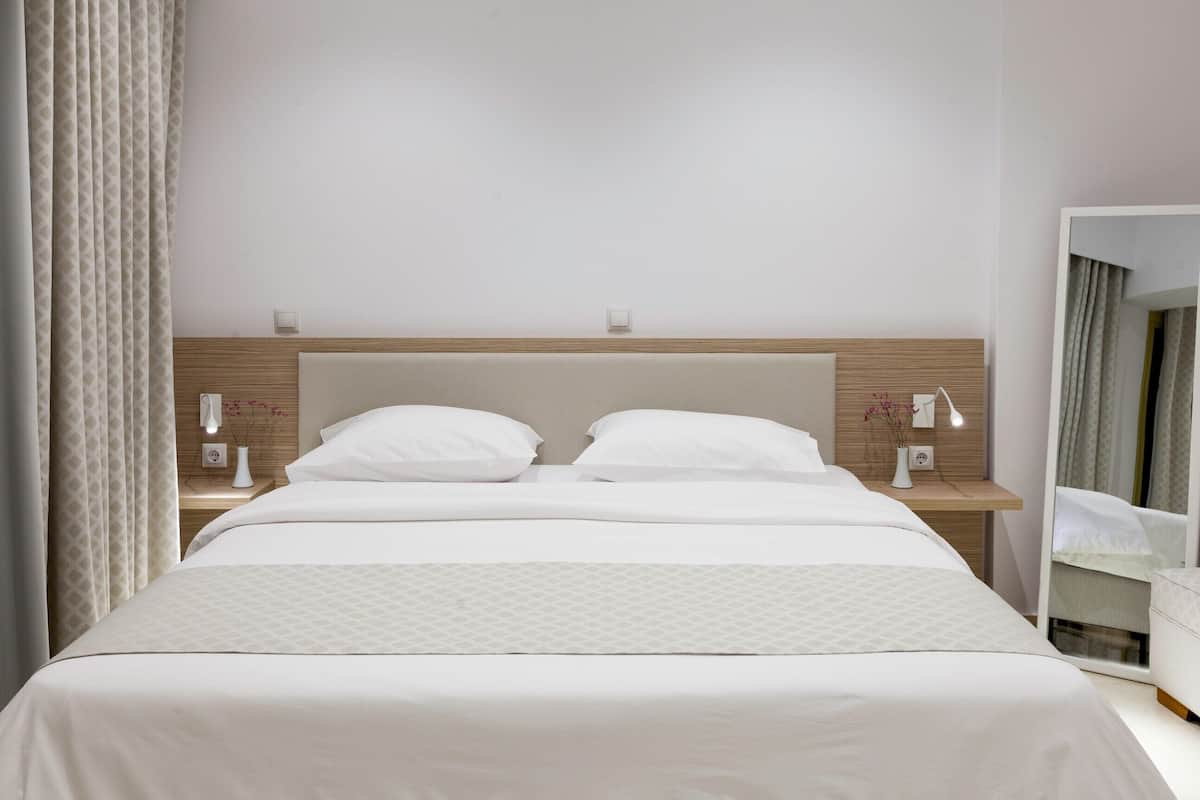 A neatly made bed with white linens, a wooden headboard, bedside tables with lamps, and a mirror on the wall.